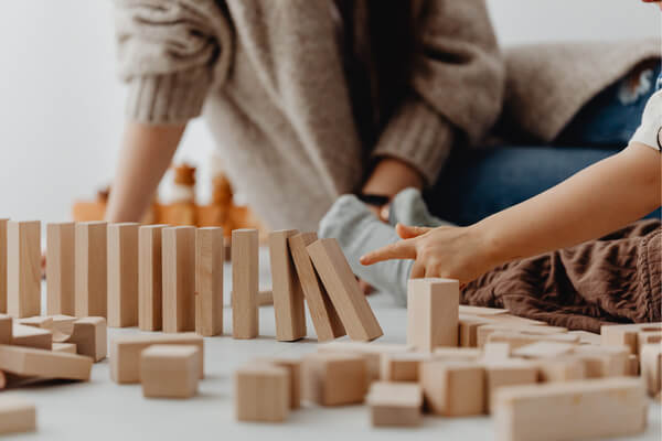 Adult and child playing with blocks set up like dominos