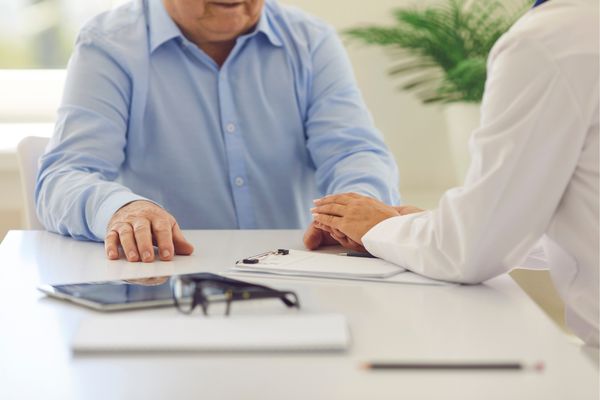 Woman placing comforting hands on elderly man's hand in office